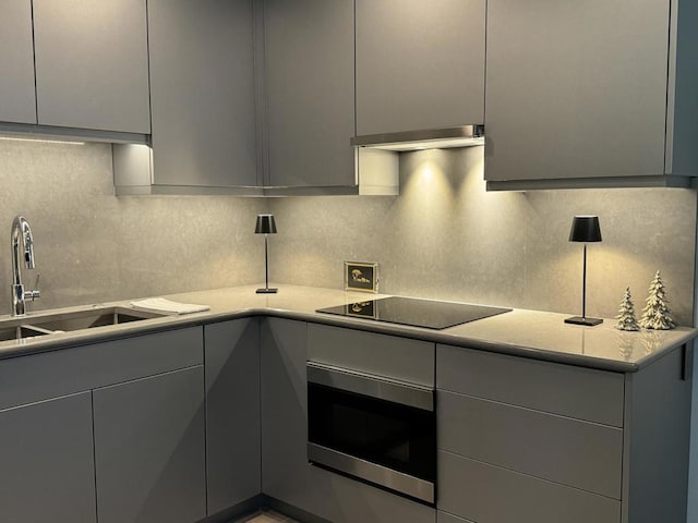 kitchen with gray cabinets, black electric stovetop, decorative backsplash, oven, and sink