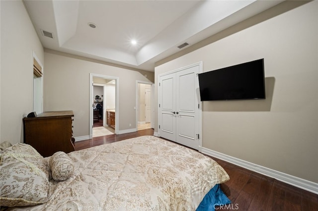 bedroom with connected bathroom, a tray ceiling, a closet, and dark hardwood / wood-style flooring