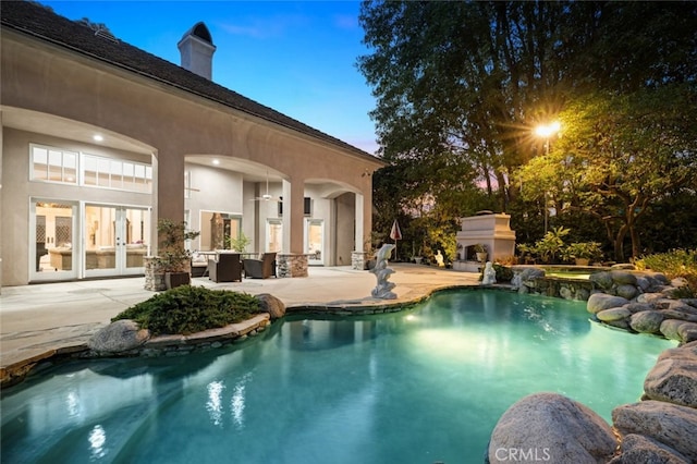 pool at dusk with an outdoor fireplace and a patio area