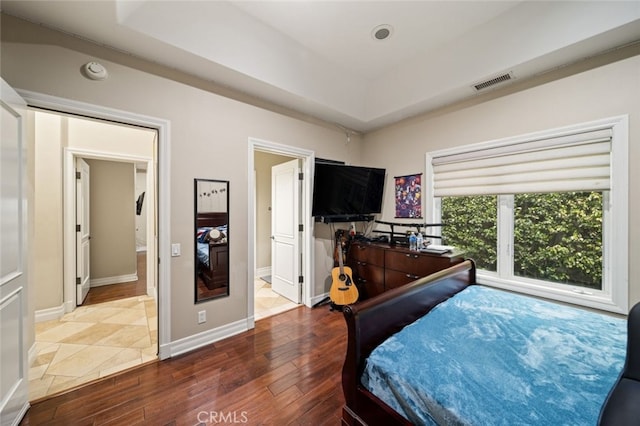 bedroom with wood-type flooring, a tray ceiling, and connected bathroom