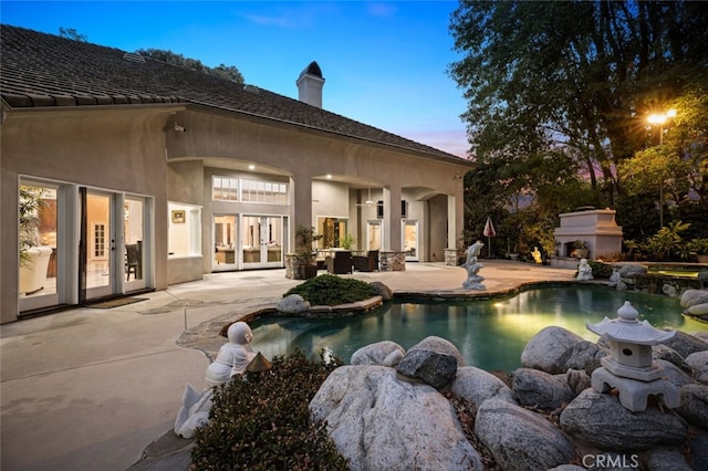 pool at dusk featuring french doors, an outdoor fireplace, and a patio area