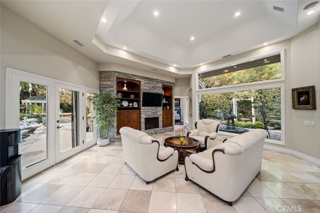 living room with french doors, a tray ceiling, light tile patterned floors, and a fireplace