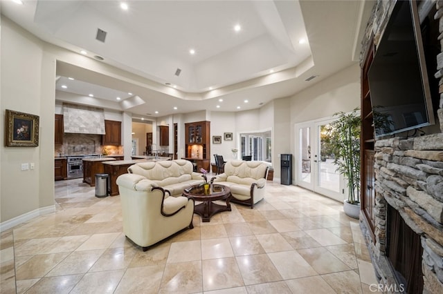 tiled living room featuring a raised ceiling, a fireplace, a towering ceiling, and french doors