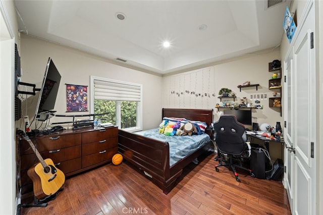 bedroom with wood-type flooring and a raised ceiling