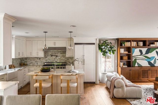 kitchen with white built in refrigerator, light stone counters, light hardwood / wood-style floors, decorative light fixtures, and a kitchen bar