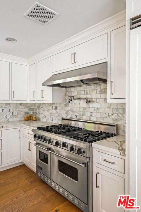 kitchen featuring backsplash, range with two ovens, wood-type flooring, light stone counters, and white cabinetry