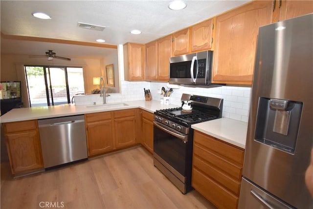 kitchen with sink, tasteful backsplash, kitchen peninsula, appliances with stainless steel finishes, and light wood-type flooring