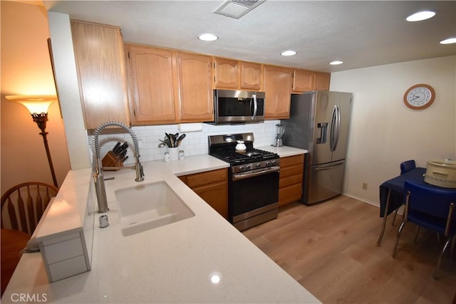 kitchen with appliances with stainless steel finishes, backsplash, light hardwood / wood-style flooring, and sink