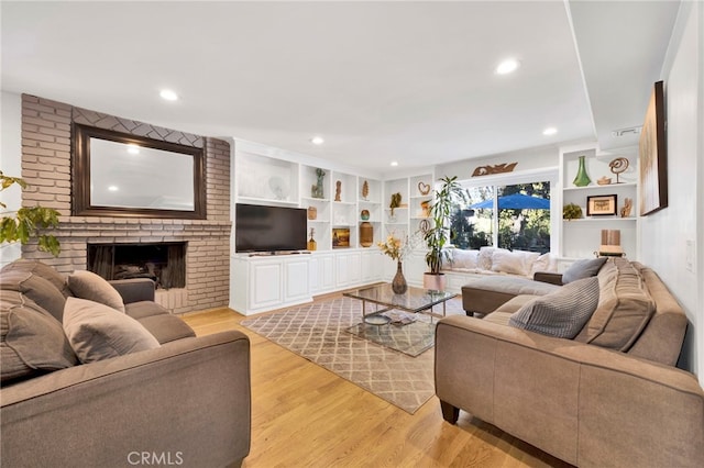 living room with light wood-type flooring, a fireplace, and built in shelves