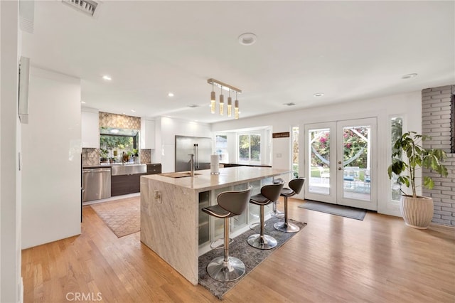 kitchen featuring light hardwood / wood-style floors, light stone counters, white cabinets, dishwasher, and a kitchen island with sink