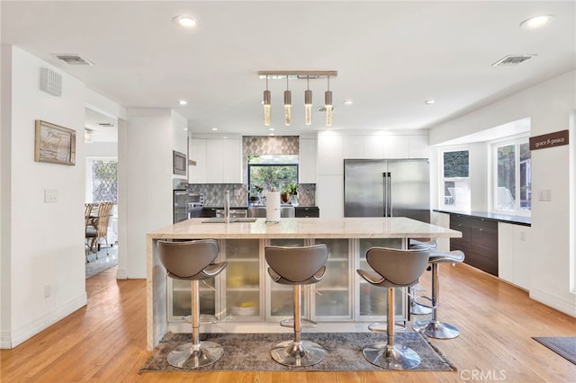 kitchen with appliances with stainless steel finishes, plenty of natural light, light hardwood / wood-style floors, and white cabinetry