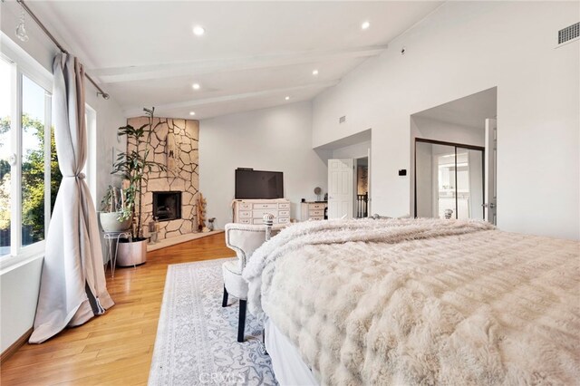 bedroom with a closet, light hardwood / wood-style floors, beamed ceiling, and a fireplace