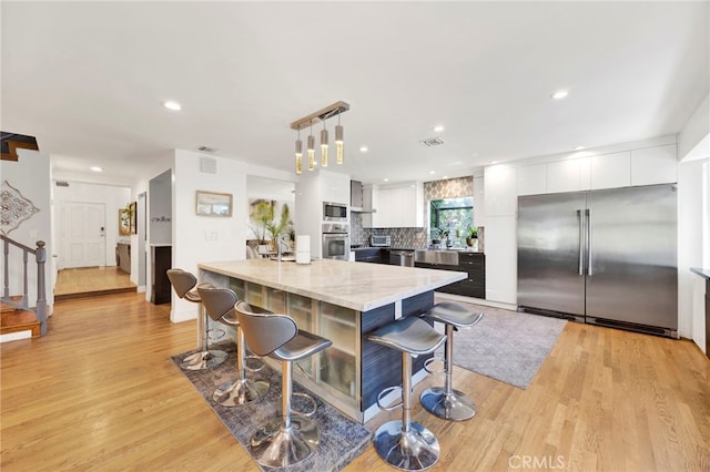 kitchen with hanging light fixtures, white cabinetry, built in appliances, a kitchen breakfast bar, and light hardwood / wood-style floors