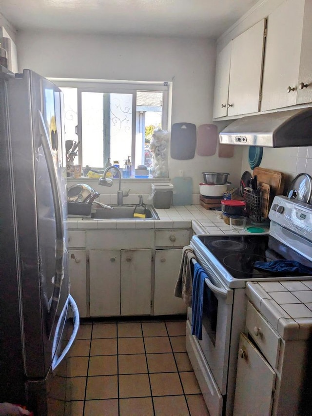 kitchen featuring white electric range, white cabinets, tile counters, and stainless steel refrigerator