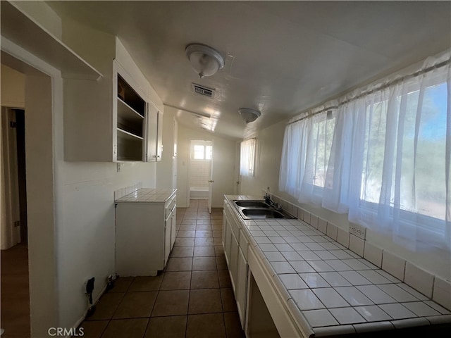 kitchen with dark tile patterned flooring, tile counters, sink, white cabinets, and vaulted ceiling