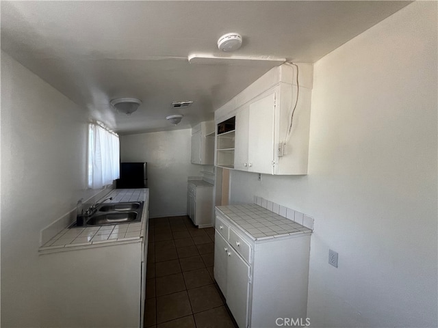 kitchen with white cabinets, washer / dryer, dark tile patterned floors, tile counters, and sink