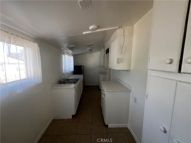 kitchen with dark tile patterned flooring, white cabinets, tile countertops, stove, and sink