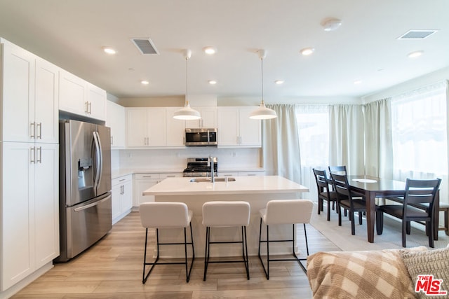 kitchen with appliances with stainless steel finishes, light wood-type flooring, sink, white cabinetry, and hanging light fixtures