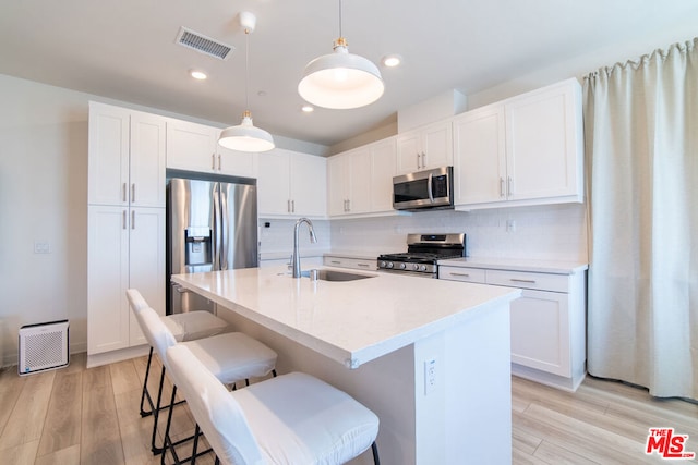 kitchen with a center island with sink, hanging light fixtures, sink, light hardwood / wood-style flooring, and appliances with stainless steel finishes