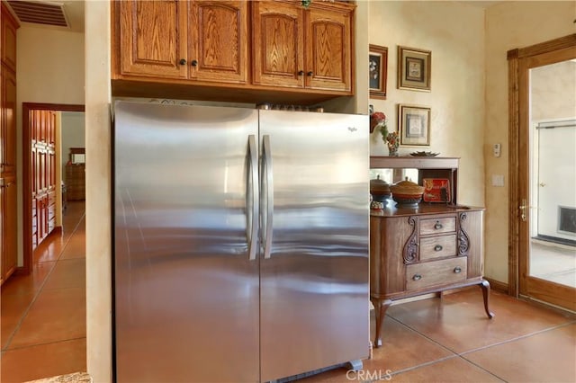 kitchen with freestanding refrigerator, light tile patterned floors, brown cabinets, and visible vents
