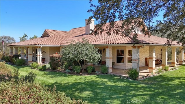 rear view of property featuring a tile roof, a lawn, a patio, and a chimney