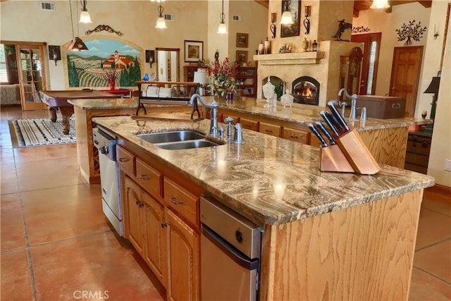 kitchen featuring a lit fireplace, a sink, a large island with sink, stainless steel dishwasher, and light tile patterned floors
