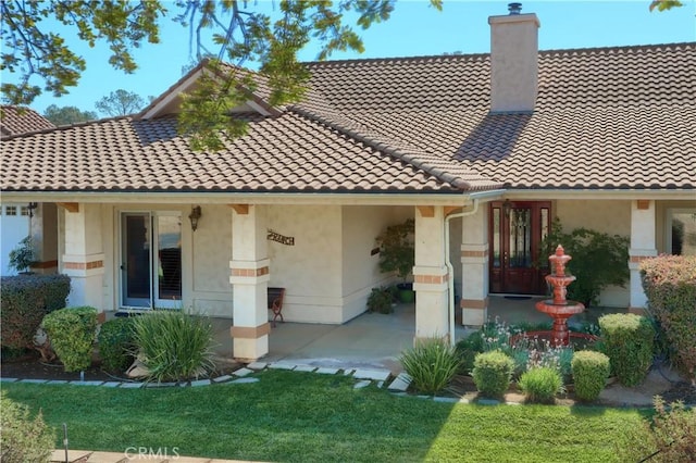 rear view of property featuring a chimney, stucco siding, and a tile roof
