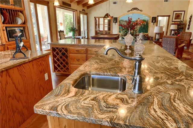 kitchen with decorative light fixtures, vaulted ceiling, a sink, light stone counters, and visible vents