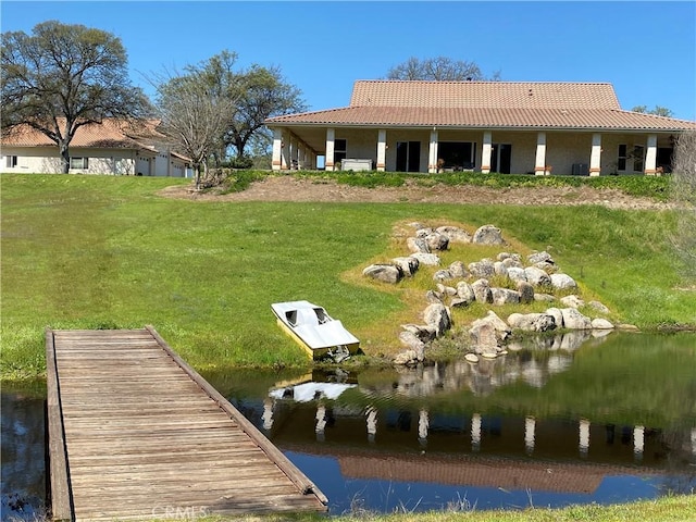 rear view of property featuring a lawn, a water view, and a tiled roof
