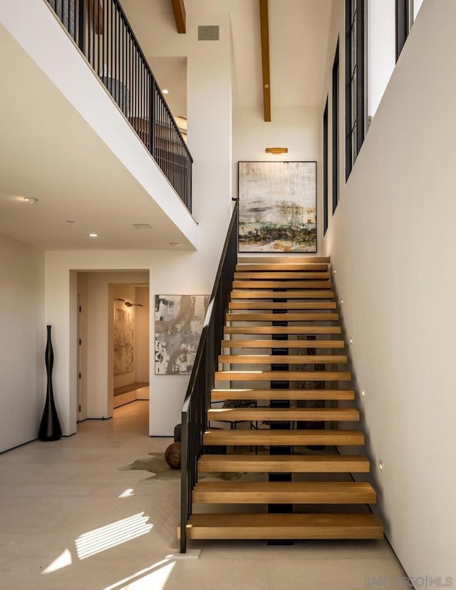 staircase featuring a towering ceiling and beamed ceiling