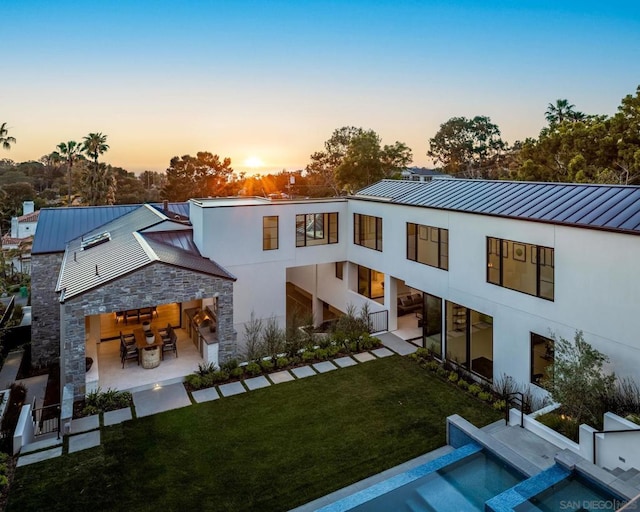 back house at dusk featuring a lawn and a patio area