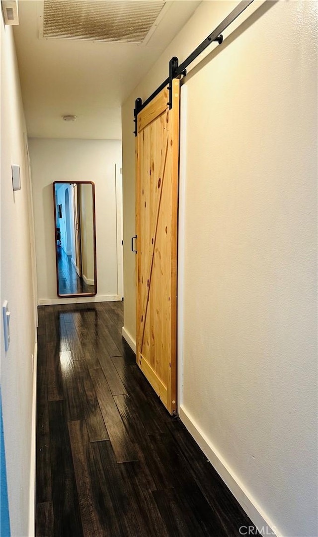 hallway with dark wood-type flooring and a barn door