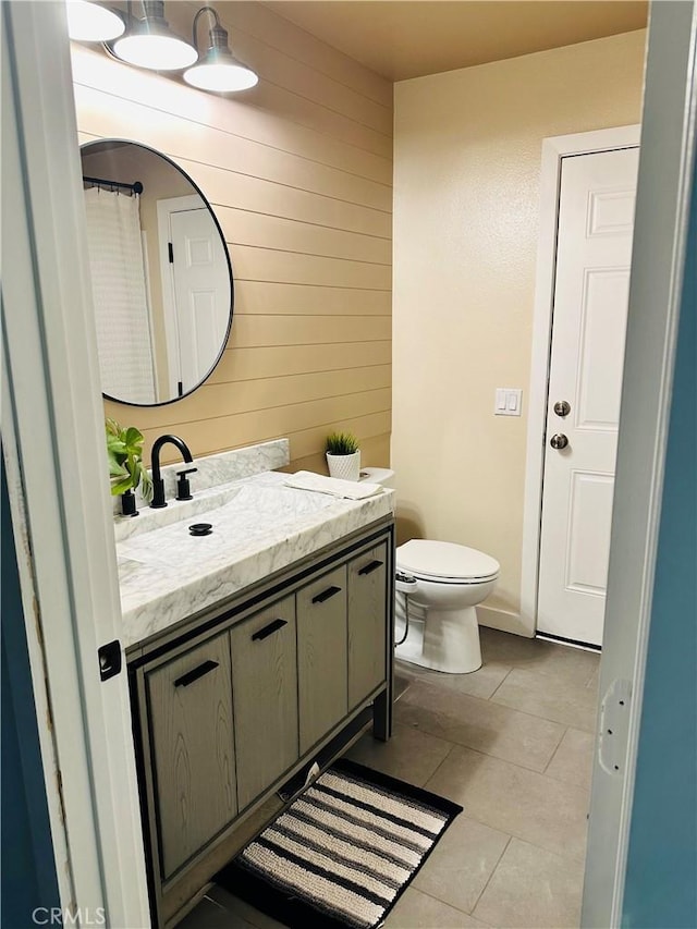 bathroom featuring toilet, vanity, tile patterned flooring, and wooden walls