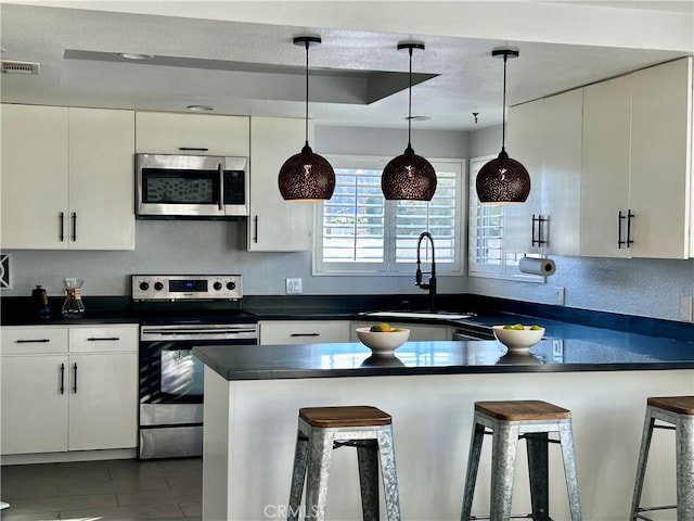 kitchen featuring pendant lighting, a kitchen bar, sink, appliances with stainless steel finishes, and white cabinets