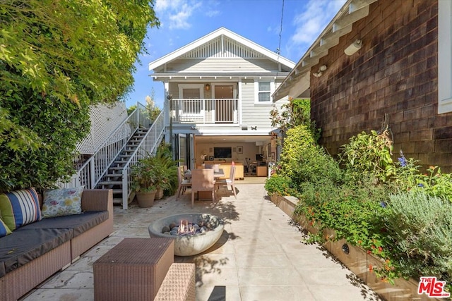 rear view of property featuring an outdoor living space with a fire pit, a balcony, and a patio