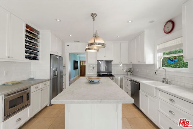 kitchen with white cabinetry, appliances with stainless steel finishes, decorative light fixtures, a kitchen island, and sink