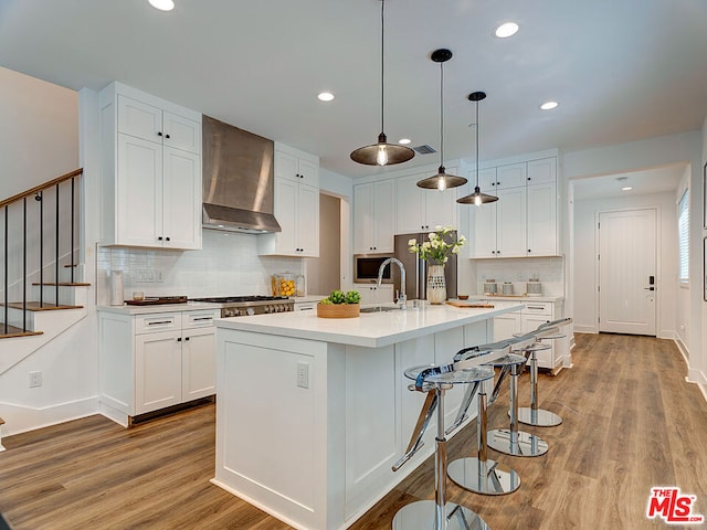 kitchen with light wood-type flooring, pendant lighting, wall chimney range hood, and white cabinets