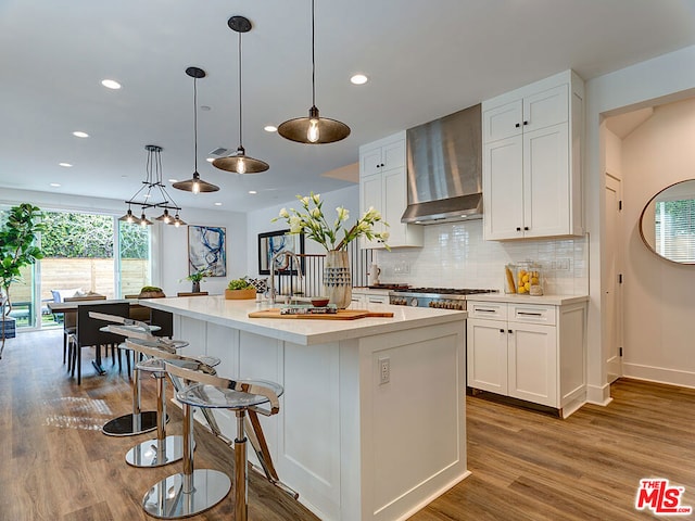 kitchen featuring a kitchen island with sink, wall chimney exhaust hood, white cabinetry, and hardwood / wood-style flooring