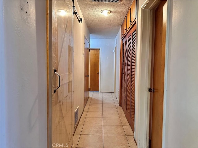 hallway with a textured ceiling and light tile patterned flooring