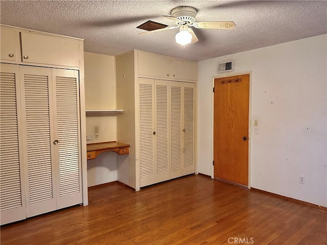 unfurnished bedroom with wood-type flooring, built in desk, a textured ceiling, and ceiling fan