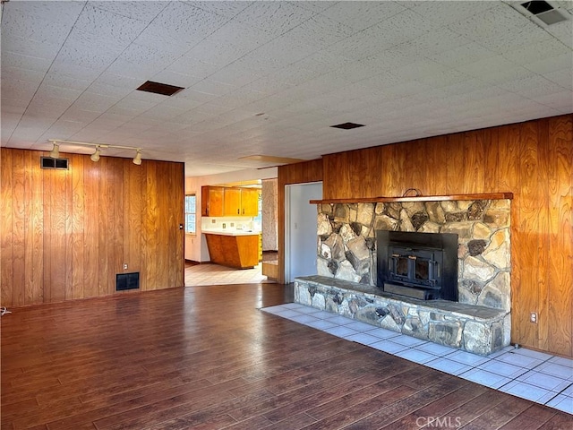 unfurnished living room featuring wood-type flooring, rail lighting, wooden walls, and a wood stove