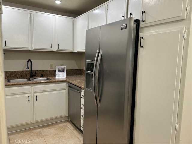 kitchen featuring sink, light tile patterned flooring, stainless steel appliances, white cabinets, and dark stone countertops