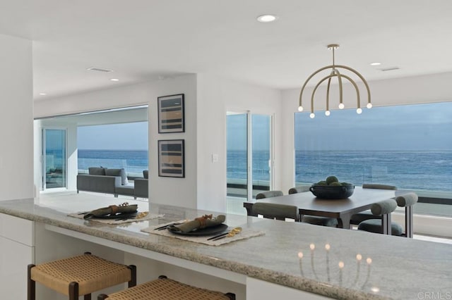 kitchen featuring a wealth of natural light, a water view, white cabinets, and decorative light fixtures