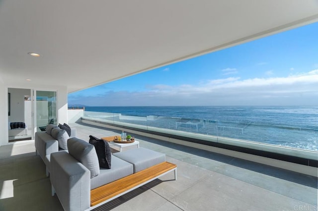 balcony with an outdoor living space, a water view, and a beach view