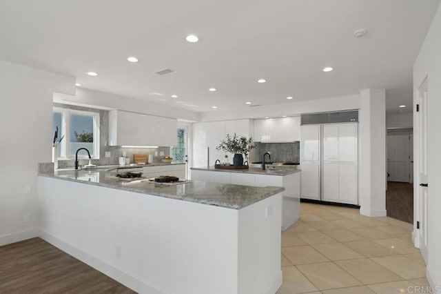 kitchen featuring tasteful backsplash, kitchen peninsula, paneled refrigerator, white cabinets, and light hardwood / wood-style flooring