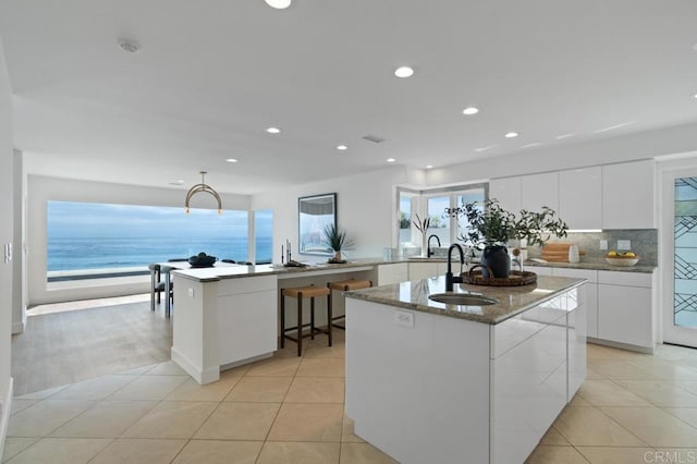 kitchen with a center island with sink, sink, a water view, and a healthy amount of sunlight