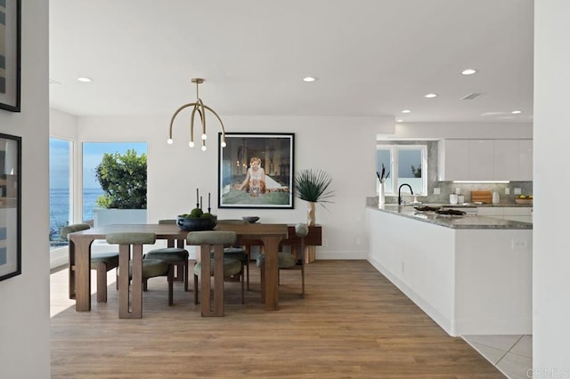 dining space with sink, light hardwood / wood-style flooring, a notable chandelier, and a water view