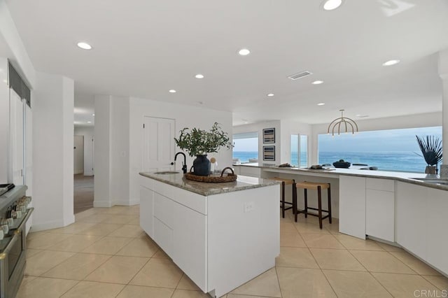 kitchen featuring white cabinets, an island with sink, stainless steel range, sink, and a water view