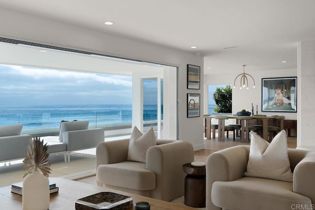 living room featuring a chandelier, a water view, light hardwood / wood-style floors, and a view of the beach