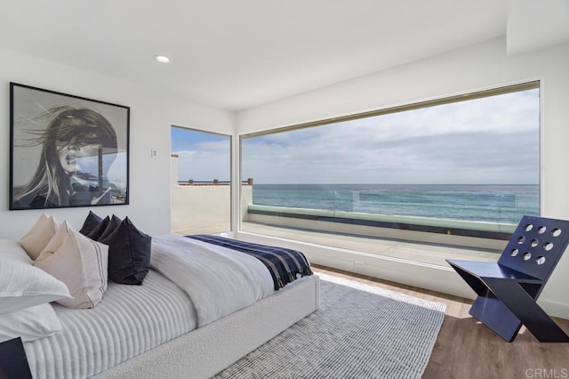 bedroom with wood-type flooring, a water view, and a beach view